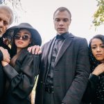 Four diverse people stand solemnly outdoors, conveying emotion and connection.