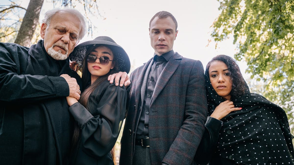 Four diverse people stand solemnly outdoors, conveying emotion and connection.